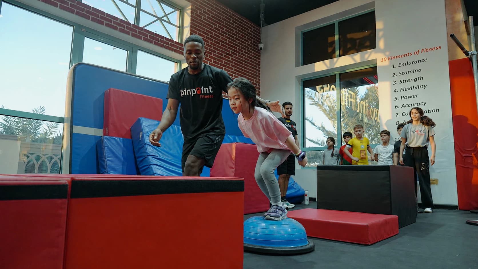 A coach guiding a child balancing on a bosu ball at Pinpoint Fitness